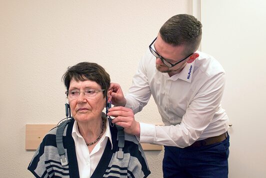 Ein Hörakustiker passt einer älteren Frau ein Hörgerät im Hörstudio an.