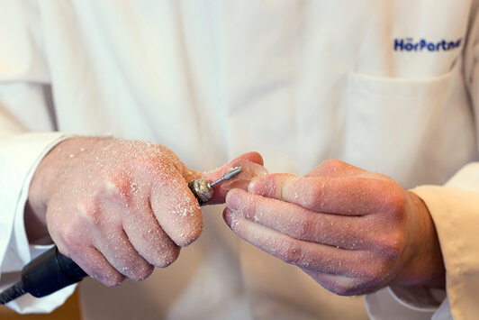 Ein Hörakustiker schleift ein Hörgerät mit einem Fräser zur individuellen Anpassung.